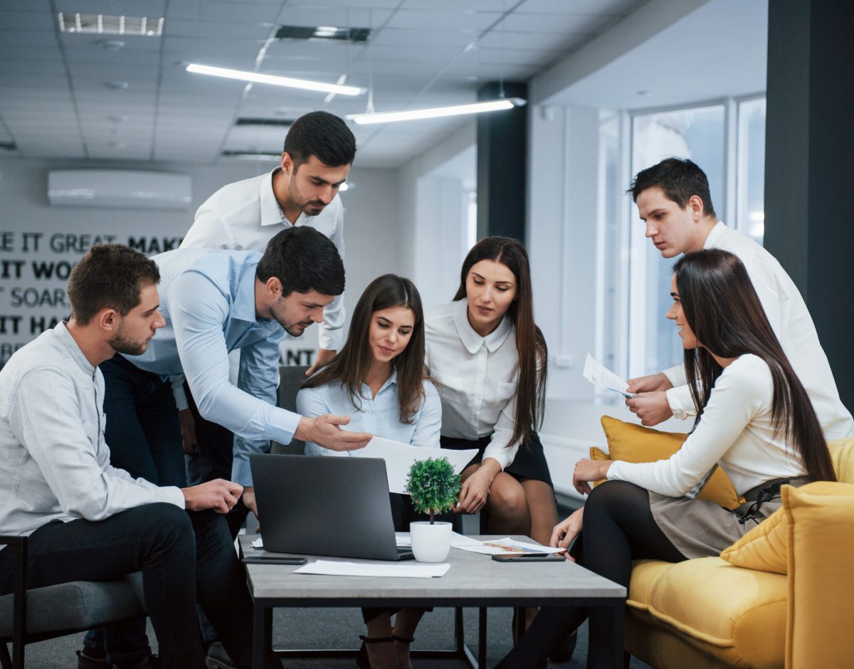 Guy shows document to a girl. Group of young freelancers in the office have conversation and working.